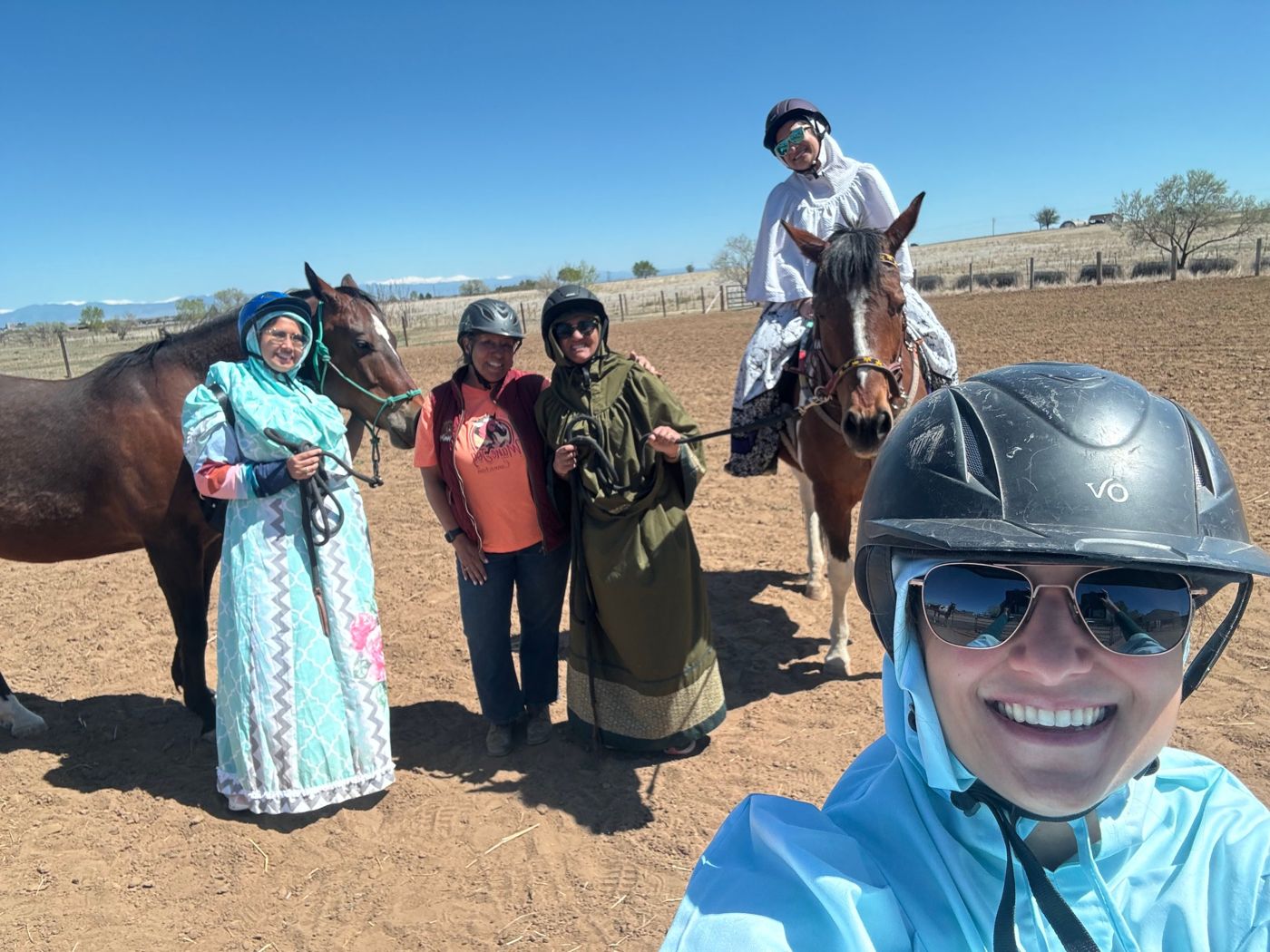 A group of herd members in pioneer dresses and helmets posing with horses on a sunny day