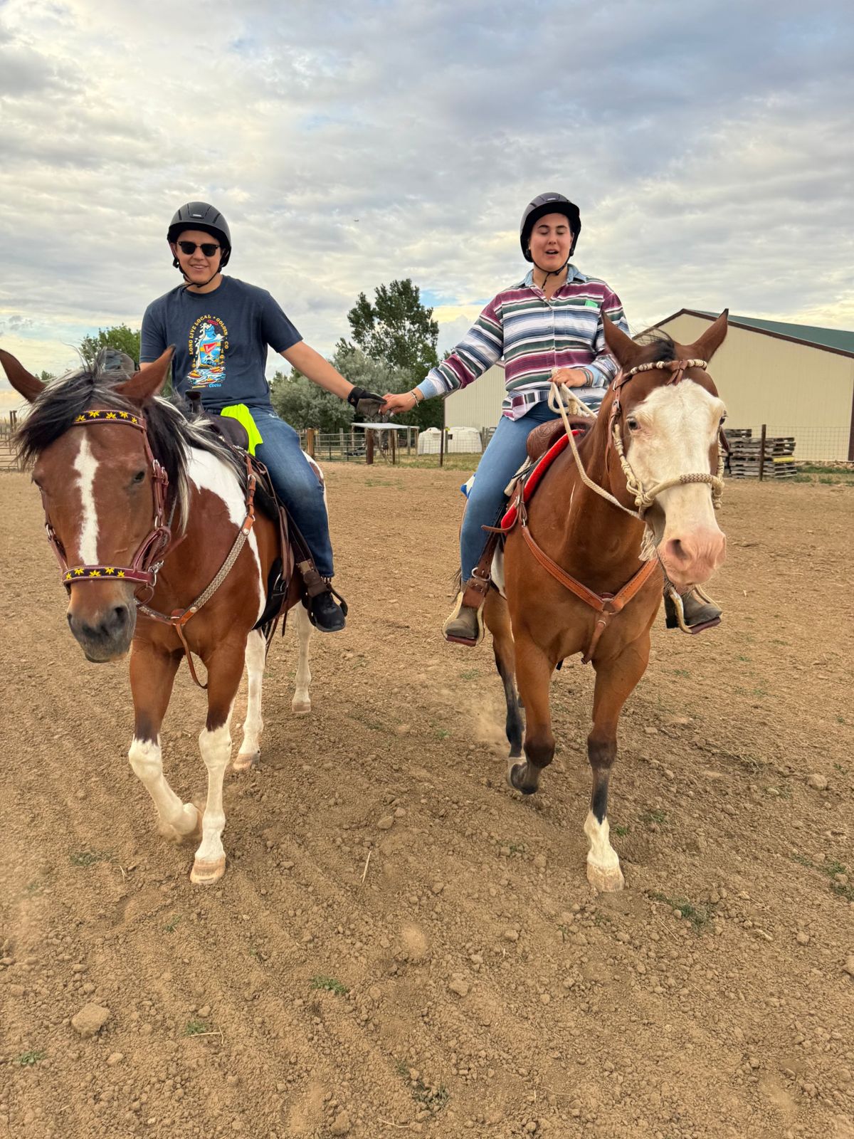 Two smiling riders holding hands on horseback in the arena