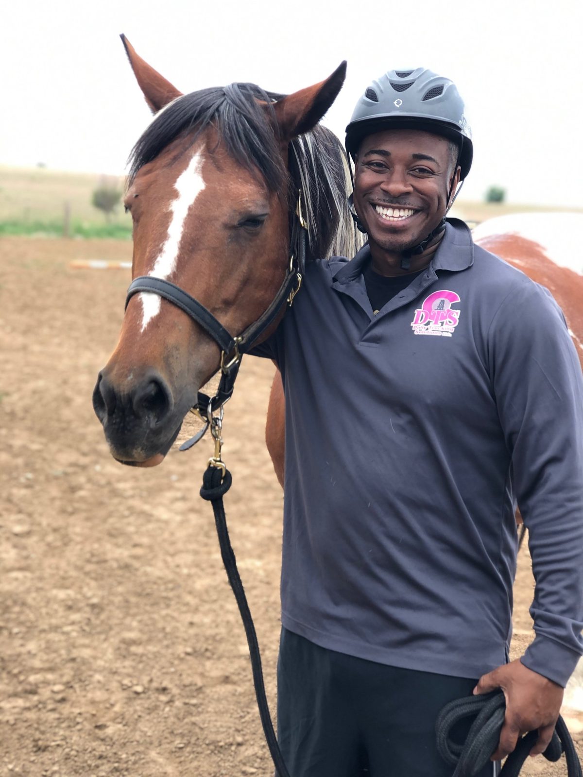 A smiling rider in a helmet standing cheek to cheek with Bourbon