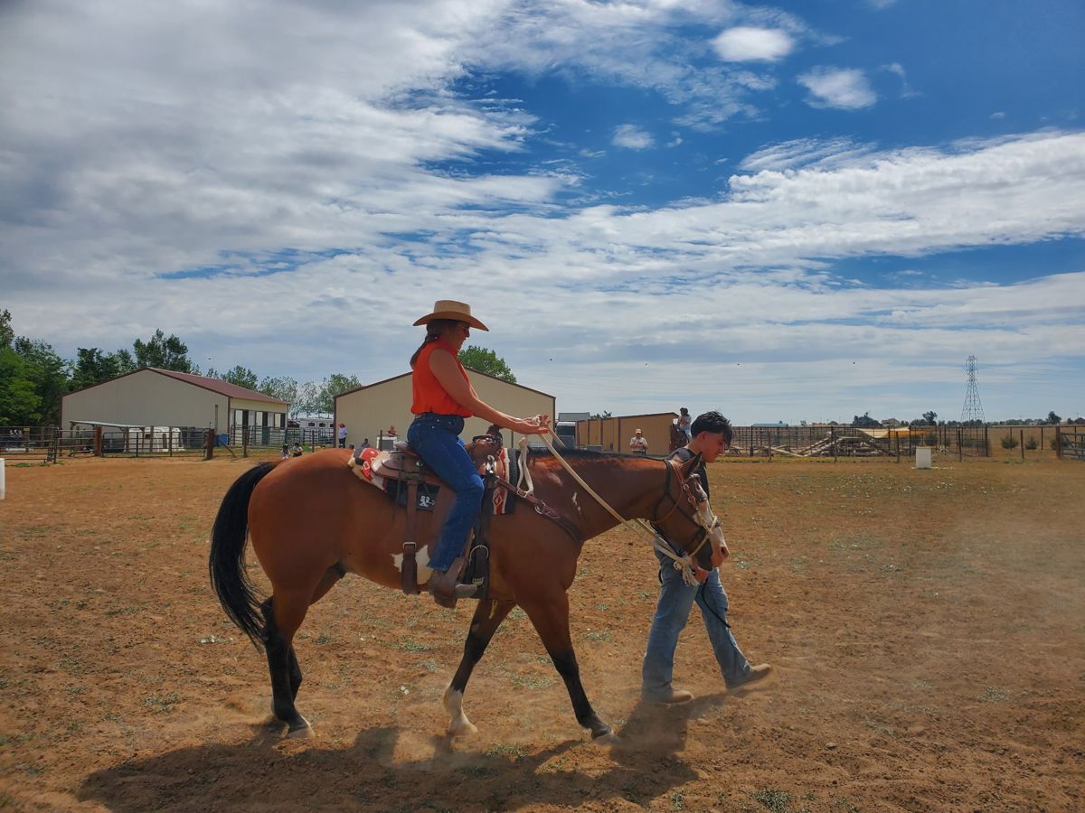 A rider in a cowboy hat on a bay horse being led around the arena under a big blue sky